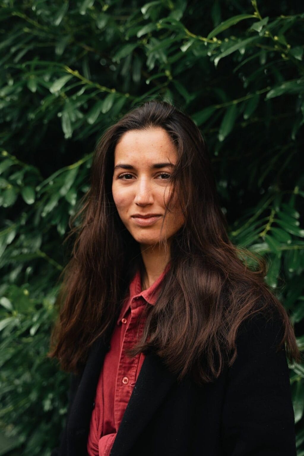 Portretfoto van Eline Bodha, regisseur van theatervoorstelling Door Mijn Bruine Ogen. Ze draagt een zwarte jas met daaronder een rood overhemd.