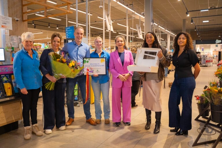 Groepsfoto van personeel van AH XL, wethouder Nathalie Kramers, Marem (van Tûmba) en Jaleesa Schiphorst (Beleidsadviseur Diversiteit & Inclusie) met hierop een aantal dingen die het team van Albert Heijn XL heeft ontvangen. Een taart, bos bloemen en de oorkonde met hierop 'Winnaar Diversiteitsprijs 2025'